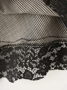 Detailed close-up of houndstooth fabric with delicate black floral lace stitching