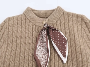 Dettaglio maglione a trecce color cammello con bottone dorato e sciarpa in seta paisley