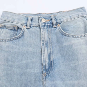 Détails de la taille d'un jean bleu clair délavé avec bouton métallique et passants de ceinture
