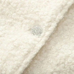 Detail of creamy white tweed jacket with premium rhinestone button and textured wool fabric