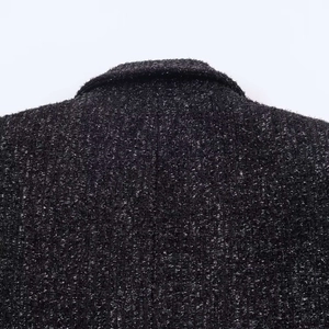 Detailed close-up of black tweed fabric texture with metallic thread on blazer collar