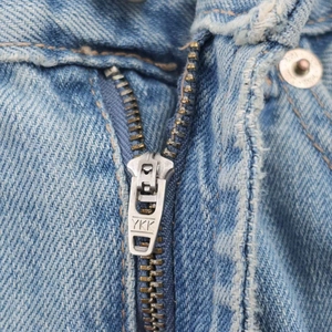 Détail de la fermeture éclair YKK en métal sur un jean vintage avec bords effilochés