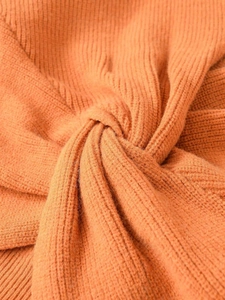 Detailed close-up of orange ribbed knit sweater featuring a stylish twisted knot design
