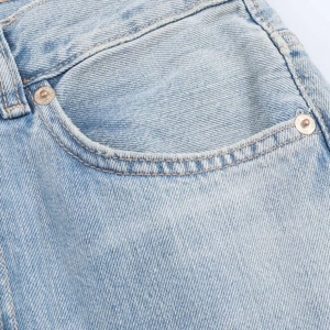 Détail d'une poche en jean bleu clair avec coutures orange et rivets en métal