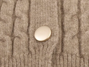 Dettaglio macro della maglia a treccia marrone con bottone dorato e bordo a costine