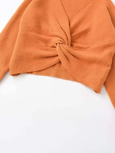 Detail of orange knitted sweater showing a stylish cross-knot V-neck design and fine texture