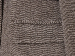 Détail du tissu du blazer en laine à chevrons avec coutures précises et texture grise