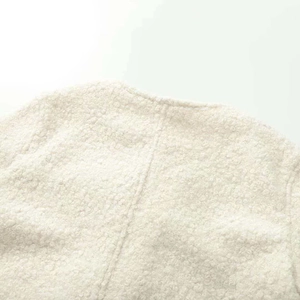 Close-up detail of cream bouclé fabric jacket showing round neck collar and stitching seam