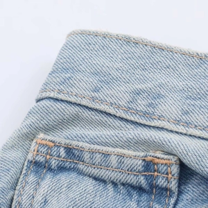 Détail d'un jean bleu clair montrant les coutures de la taille et la poche soignée