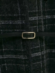 Détail d'un manteau en maille à carreaux avec une ceinture noire et boucle dorée