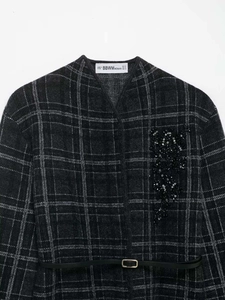Détail d'un manteau en maille à carreaux gris foncé avec broderie de perles et ceinture fine