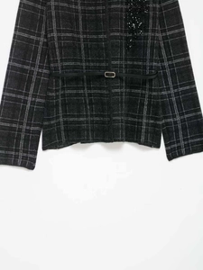 Détail d'une veste en tricot gris à carreaux avec broderie de perles et ceinture noire