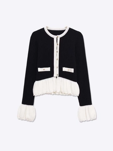 Détail du cardigan en maille avec boutons dorés élégants et ourlet blanc volanté