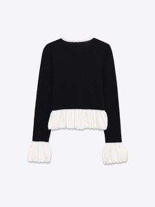 Détail du pull en maille avec tricot noir côtelé et volants blancs aux poignets et à l'ourlet