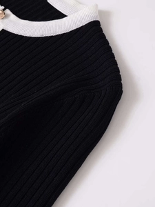 Détail du pull en maille côtelée noire avec col contrasté blanc et bouton doré élégant