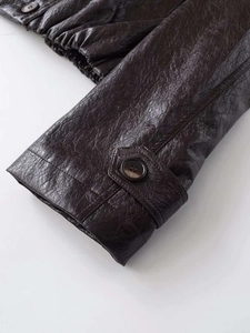 Detail of dark brown leather jacket cuff with button strap and textured grain finish