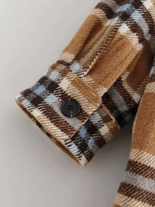 Macro shot of plaid flannel jacket cuff with brown resin button and brushed texture
