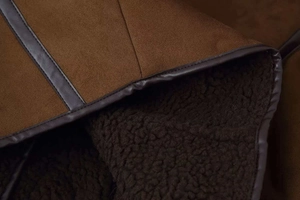 Macro view of brown faux suede jacket with thick dark brown shearling lining and leather piping