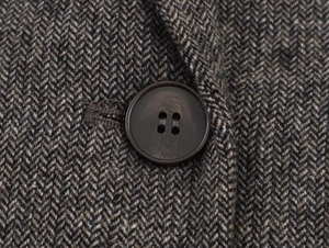 Detail of herringbone wool blazer fabric with a premium dark brown four-hole button