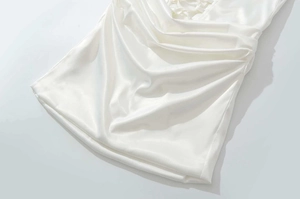 Detail of white satin dress featuring elegant pleats and intricate lace-up front design