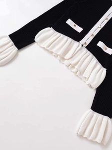 Détail du cardigan avec bouton doré et bordure à volants plissés blancs sur l'ourlet et poignets