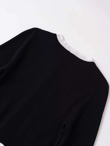 Détail d'un pull en maille côtelée noire avec col contrasté blanc et boutons dorés