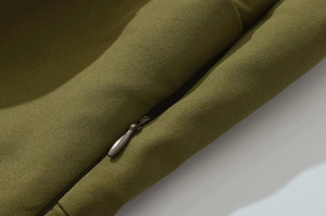Detailed view of an invisible zipper with a teardrop metal pull on olive green dress fabric