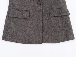 Detail of grey herringbone tweed fabric featuring flap pockets and a round dark button