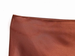 Macro detail of satin fabric texture and premium stitching on a brick red skirt