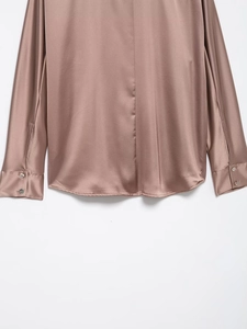 Detail shot of rose gold satin blouse featuring buttoned cuffs and curved hemline