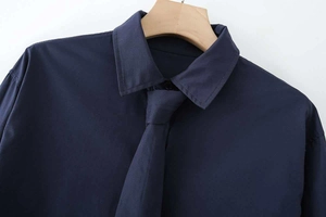 Detail of navy blue cotton poplin long sleeve shirt with matching slim tie on wooden hanger