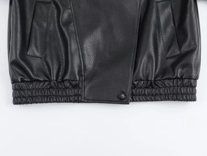 Macro detail of black leather jacket showing lychee texture and elastic pleated hemline