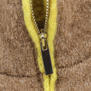 Close-up of silver metal zipper on a brown textured shearling jacket with yellow trim