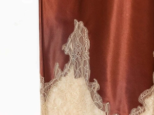 Detail of rust-red satin fabric with intricate beige lace trim on feminine skirt