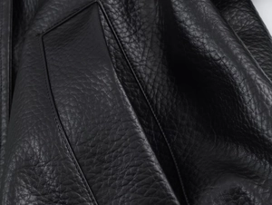 Detailed close-up of premium black litchi texture leather with fine stitching on a jacket