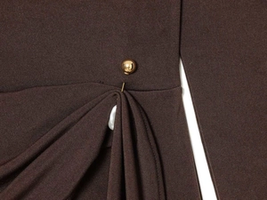 Detail of dark brown draped fabric with pleated design and a spherical gold metal buckle