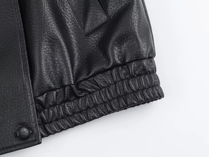 Close-up of litchi texture on black leather jacket with elastic hem and button detail