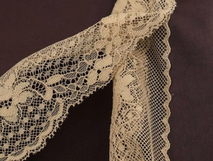 Close-up of beige lace trim with floral patterns on dark brown satin fabric detail