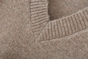 Close-up of the ribbed V-neckline and soft plush texture of the tan knitted sweater