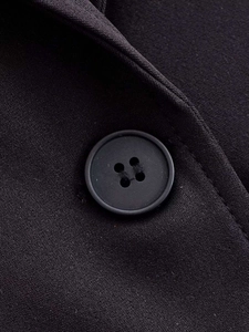 Detailed macro view of a black matte four-hole button on slim fit suit fabric texture