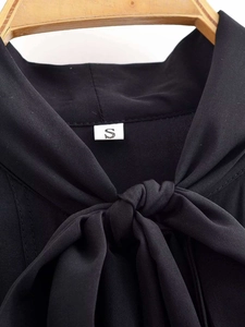 Detail of black V-neck chiffon blouse featuring a large decorative bow tie and size S label