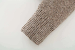 Detailed close-up of ribbed cuffs on a chunky knit V-neck sweater in camel brown