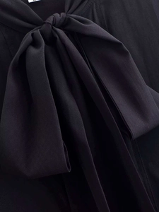 Close-up of elegant black shirt featuring a large bow tie neck design and textured fabric