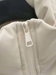 Close-up of minimalist white leather vest showing texture and matching metal zipper detail