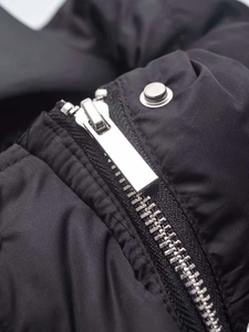 Detail of silver metal zipper and snap button on black quilted padded vest fabric