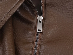 Close-up of a silver rectangular metal zipper on a brown lychee textured leather jacket