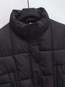 Close-up of black quilted puffer vest featuring high collar and metal snap button closure