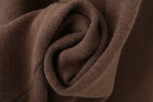Close-up of soft brown knit fabric texture on a minimalist loose V-neck cape coat