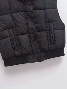 Close-up of black quilted vest featuring snap buttons, side pockets and ribbed hem