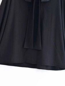Detail of a black V-neck blouse featuring a smooth polyester fabric and bow tie closure